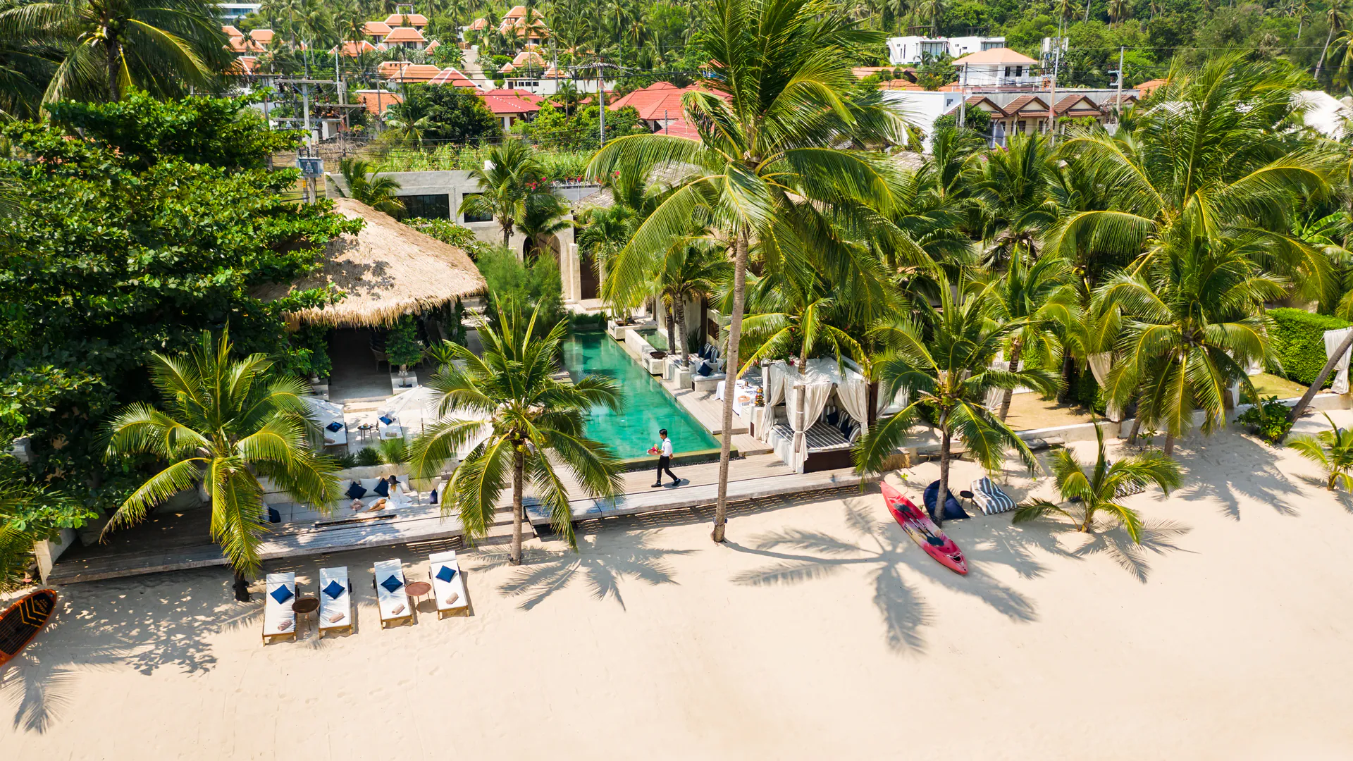 An aerial view of a luxurious beachfront villa estate featuring several interconnected homes, multiple pools, and lush tropical landscaping, redefining large group harmony with stunning ocean views.